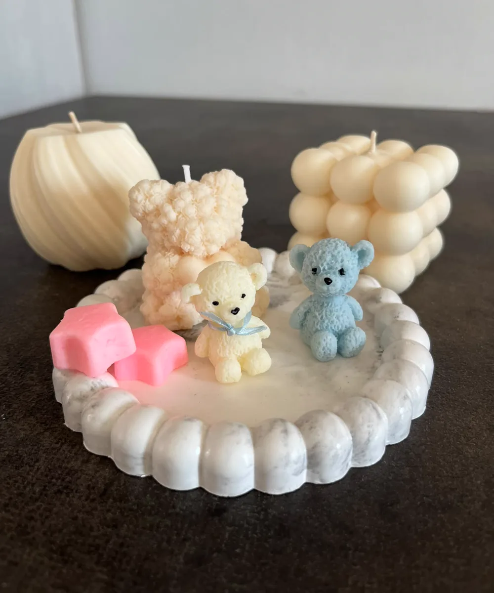 Set de velas de soja: esfera espiral, osito corazón, cubo de burbujas, ositos mini y estrellas rosas sobre una bandeja de yeso
