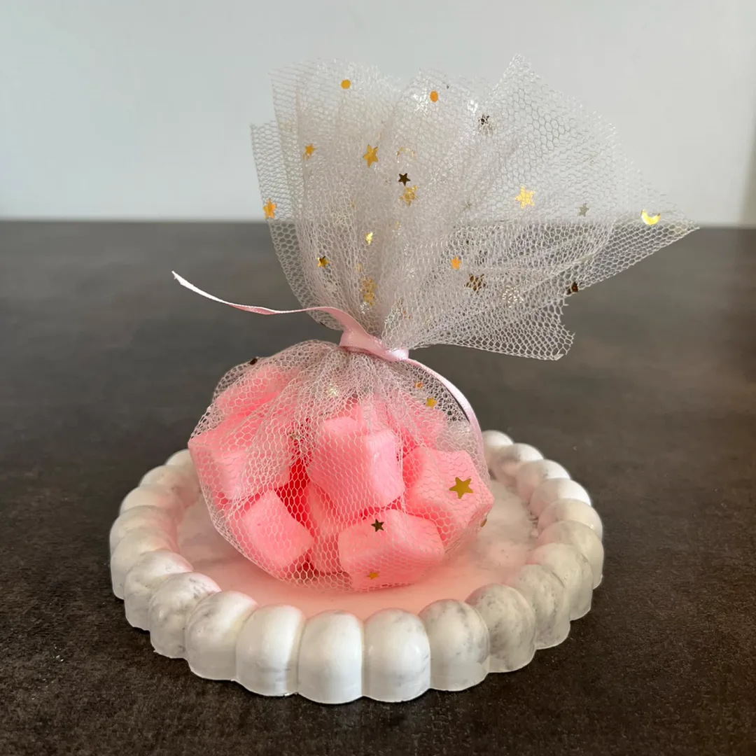 Velas de soja rosas en bolsita de tul con estrellas doradas y cinta, sobre bandeja de yeso